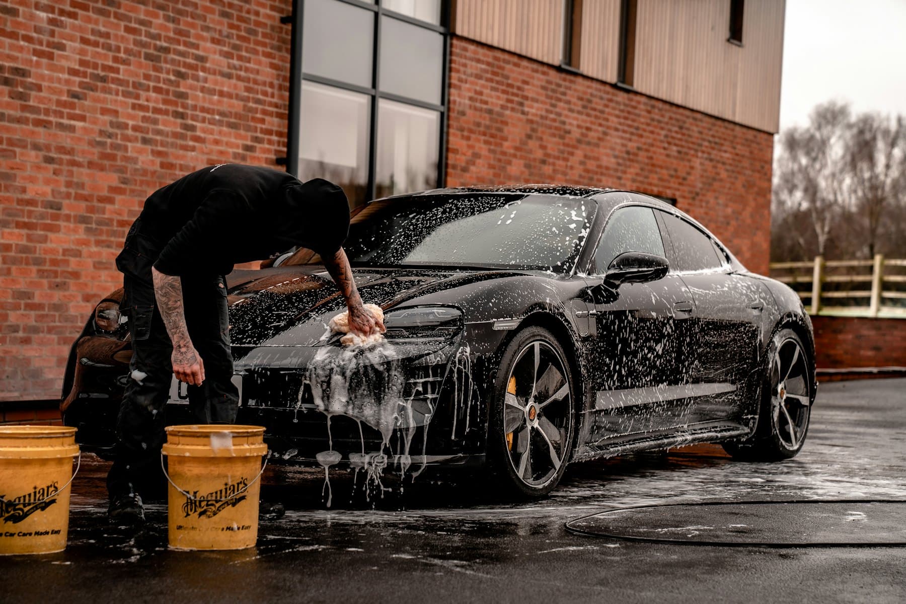 A dark sedan being washed with snow foam in a driveway